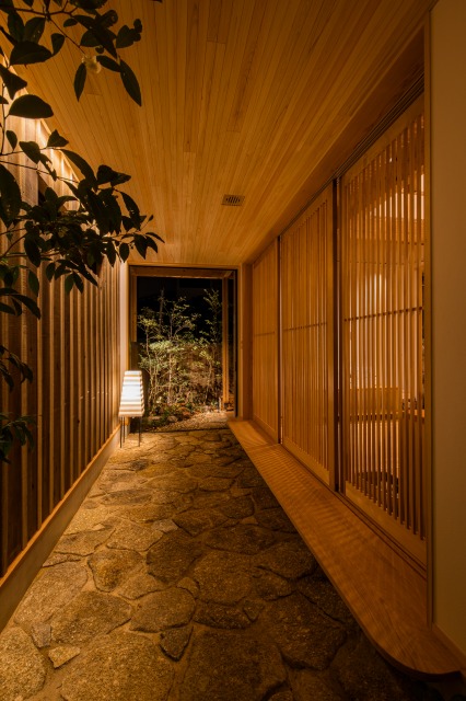 KEN建築工房｜和の風情が漂う廊下。木の格子と石畳の組み合わせが温かみを演出。外の緑がアクセントとなり、落ち着いた雰囲気を醸し出しています。