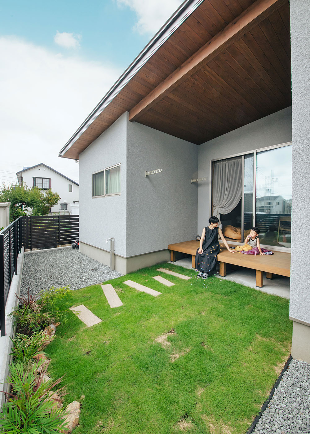 フジモクの家（富士木材）【子育て、自然素材、平屋】建物をコの字型にして、凹ませた部分にウッドデッキを設けた。そのまま芝を敷いた庭とつながり、たくさんの楽しさをもたらす。軒天にスギが張られた大きな軒が、安心感を感じさせる