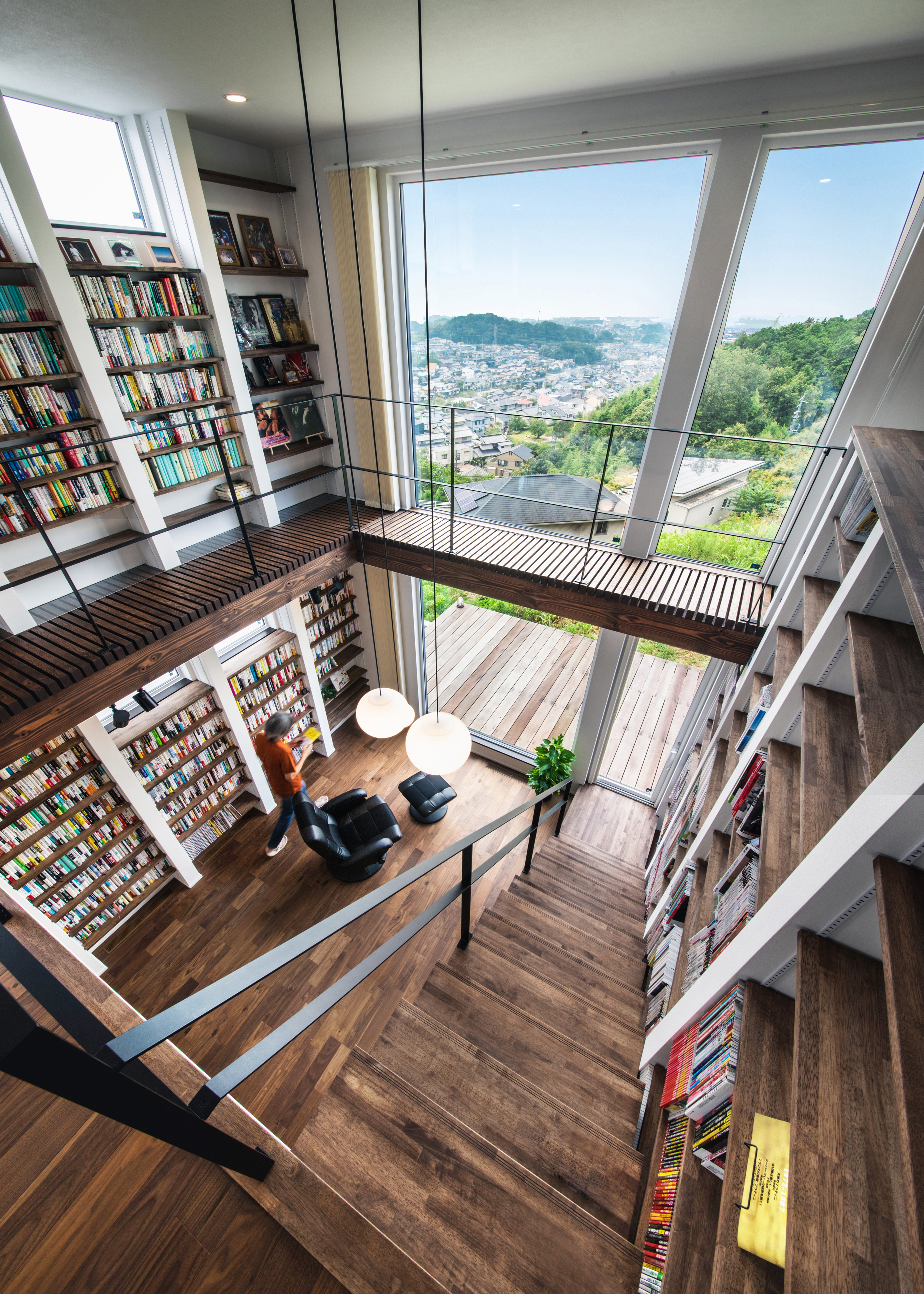 小幡建設【デザイン住宅、収納力、趣味】吹抜けのリビング。床から天井まで届く大容量の本棚を東西の壁一面に造作。大きなピクチャーウインドウから見おろす街並みの景色が、額縁で切り取られた絵画のように美しい。全館空調システムを採用したことで、これだけの大空間でも上下階の温度差がなく、一年中快適に過ごせる