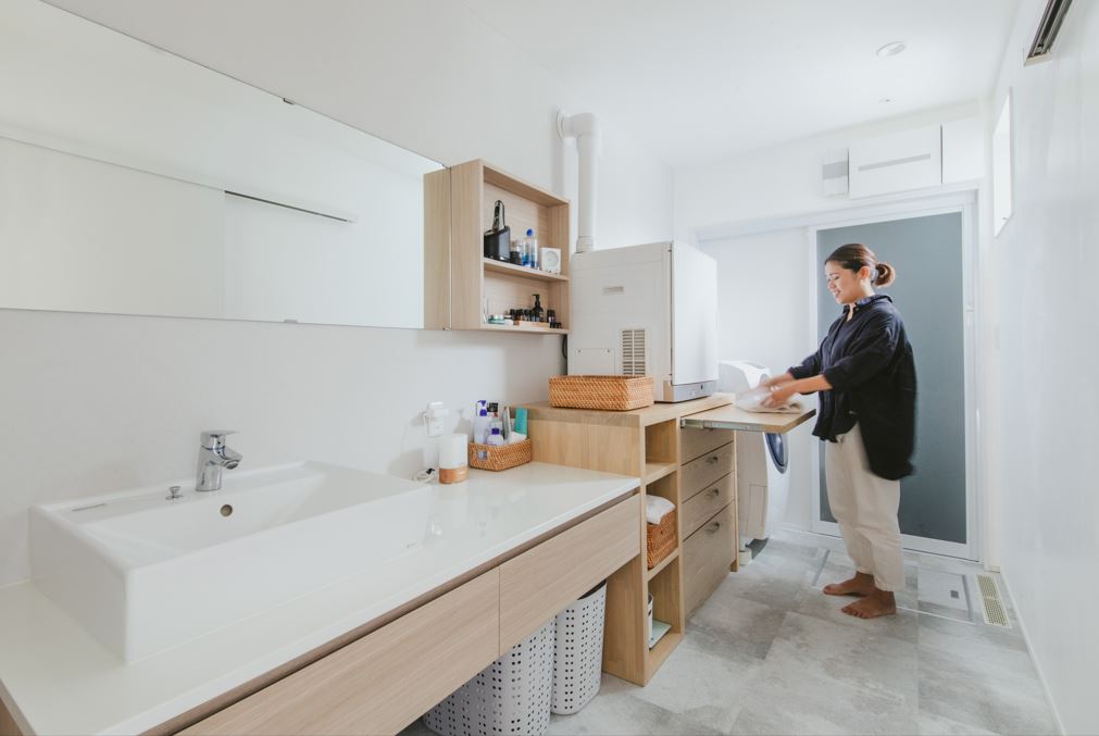 nattoku住宅【デザイン住宅、子育て、収納力】キッチンからも玄関からもスムーズにアクセスできる洗濯動線。脱衣室の収納棚にアイロン台を造作。「脱ぐ・洗う・乾かす・しまう」が一連の動きで完結できる