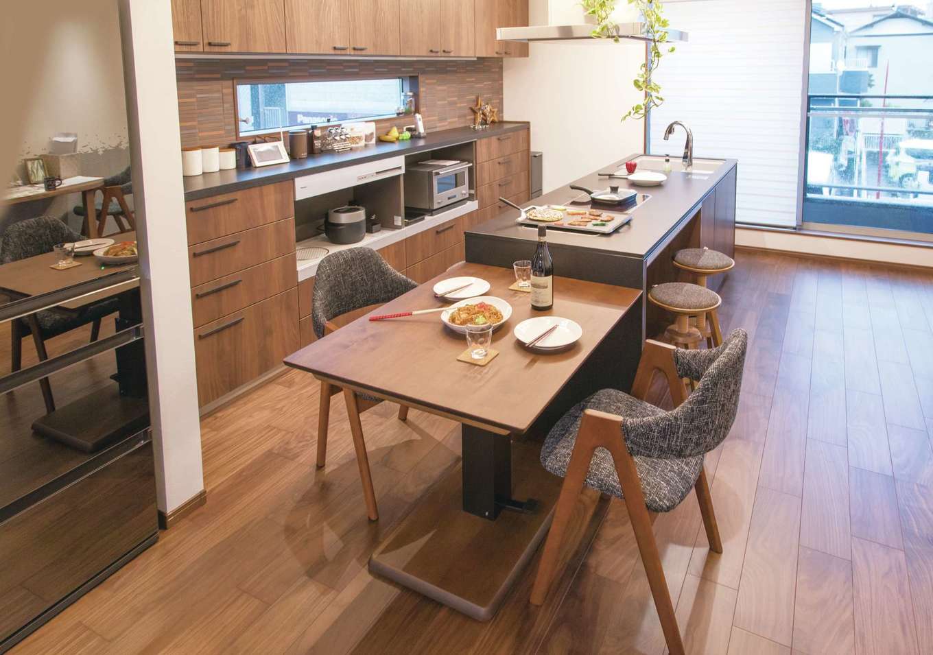建築システム（狭小住宅専門店）【浜松市中央区助信町9-16・モデルハウス】来客と一緒に食事を楽しむ時は、キッチンにテーブルを付けて。リビングのセンターテーブルは天板が昇降するタイプなので、ダイニングでの兼用が可能。こうしたアイデアの提供で、狭小住宅での暮らしやすさの提案もしている