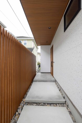 スタイリッシュなエントランスアプローチ。木製フェンスと白い壁がシンプルでモダンな印象を与え、訪れる人を温かく迎える。