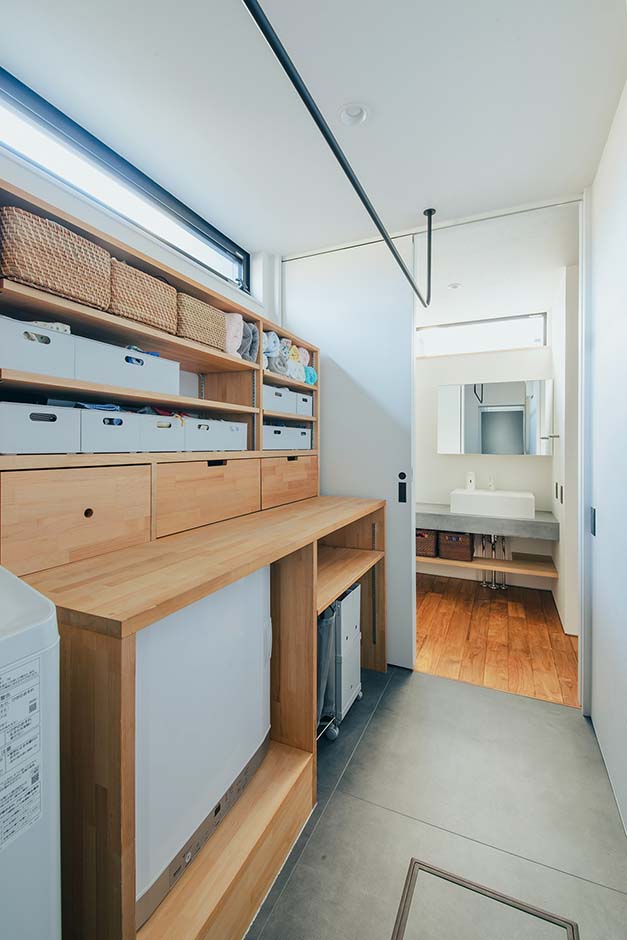 平屋建築ブルーハウス【デザイン住宅、建築家、平屋】ランドリーは、壁面に収納棚を造作し、空間を有効利用。ガス乾燥機の「乾太くん」は出し入れがしやすいように造作棚の下部分に設置した。室内干しもできるようになっていて、ファミリークローゼットも近いため、洗濯の家事動線を短縮できる