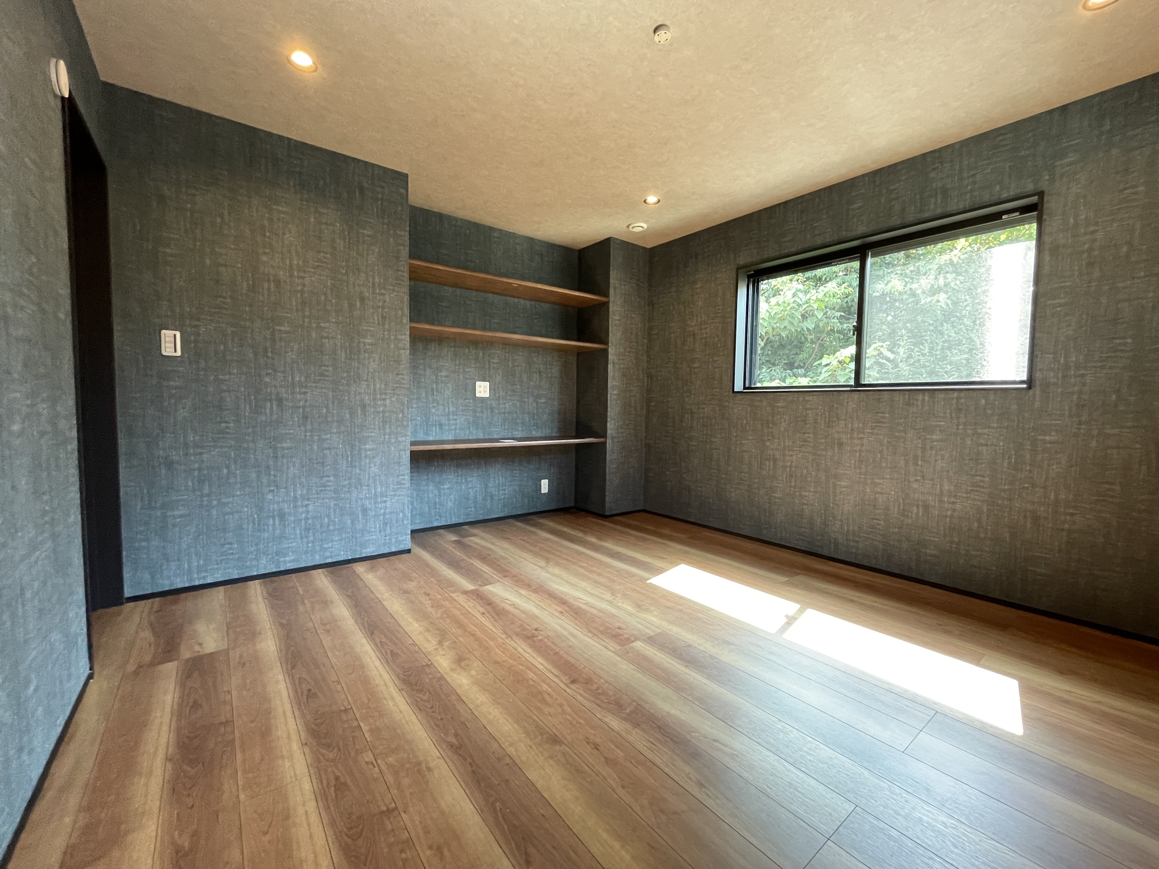 SnugStyle｜広々とした寝室は、落ち着いた雰囲気の壁紙と木目の床が特徴。自然光が室内を優しく照らし、心地よい空間を演出する。