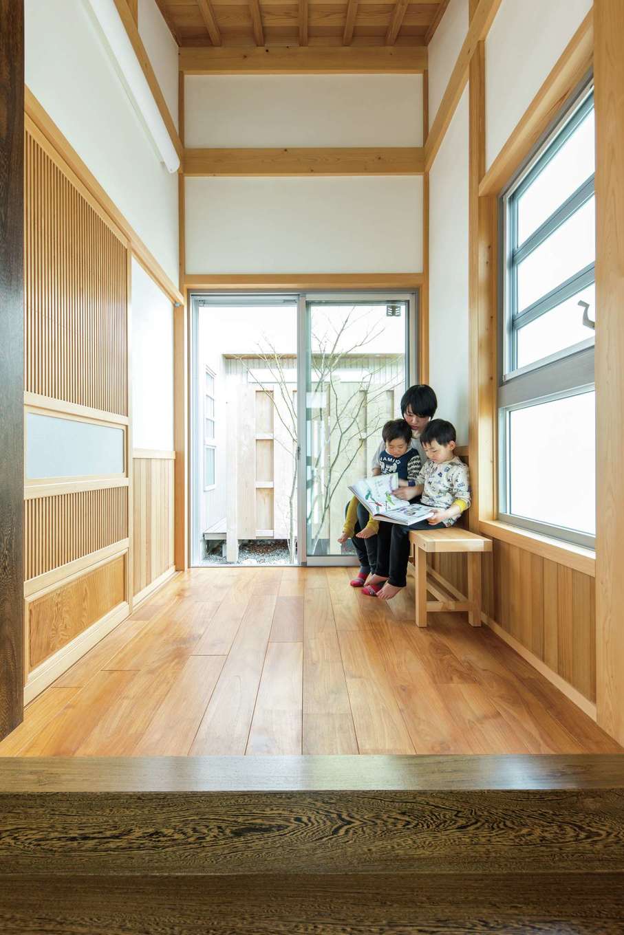 櫻 工務店【子育て】屋根勾配を活かした天井に、ガラス越しのシンボルツリー。床のチーク材はLDKより幅広の材料を使用している。手作りベンチは『櫻 工務店』からのプレゼント