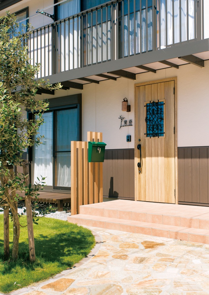 サイエンスホーム【趣味、省エネ、間取り】敷き詰めたレンガや木製のドアがかわいらしい玄関まわり。芝生のグリーンがアクセント