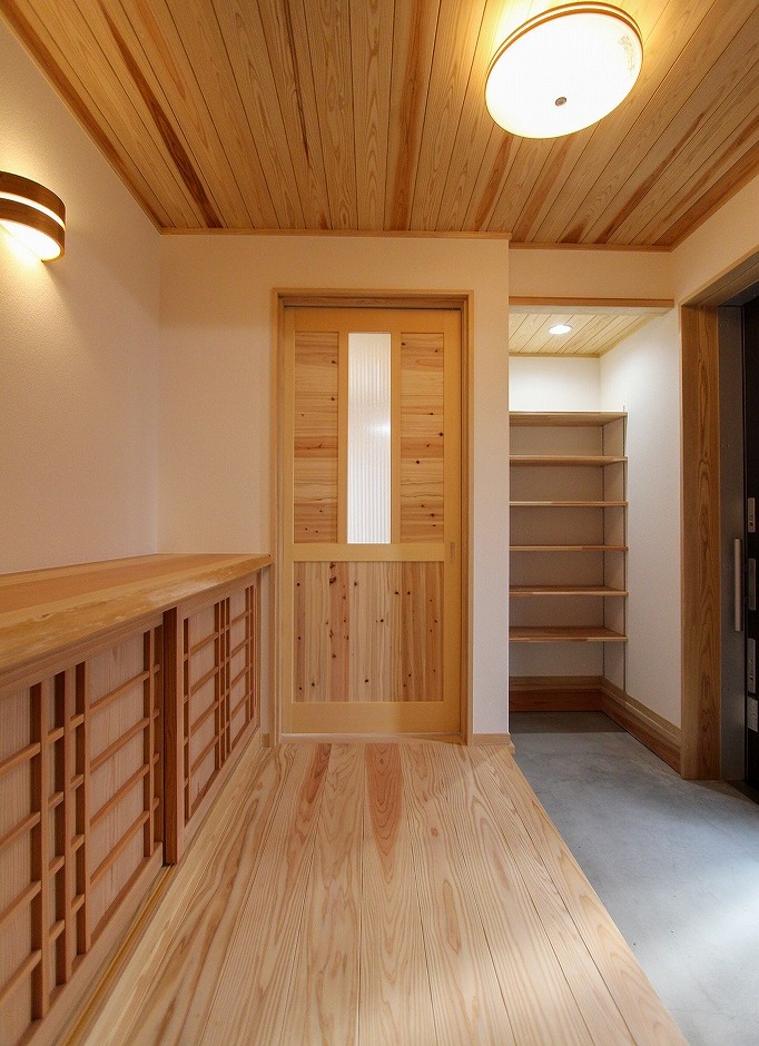 アクトホーム【自然素材、省エネ、間取り】木の香りに癒される玄関ホール。画像右手には可動棚つきの半畳の土間収納、左手には職人の手わざを活かした造り付けの下駄箱。正面の木製建具を開けると、和室につながっている。