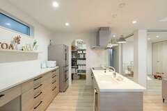 あえて吊り戸棚をやめて、スッキリとしたキッチンが完成。造作の棚は、現場で細かく打合せをして幅や高さを決定した。パントリーは可動棚による収納力はもちろん、入口のRやクロスなど希望通りの仕上がり。キッチンに立てばLDK全体が見渡せ、家族が階段を上り下りする気配も届く。右手の和室は間仕切りも可能で、幅広い用途を受け止める