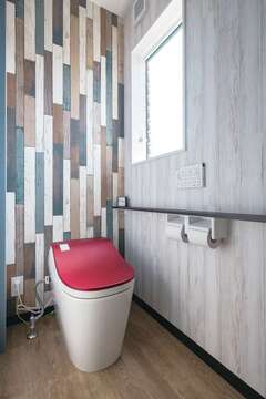 赤いふたのトイレに合わせ、壁はミックスカラーの木目調に
