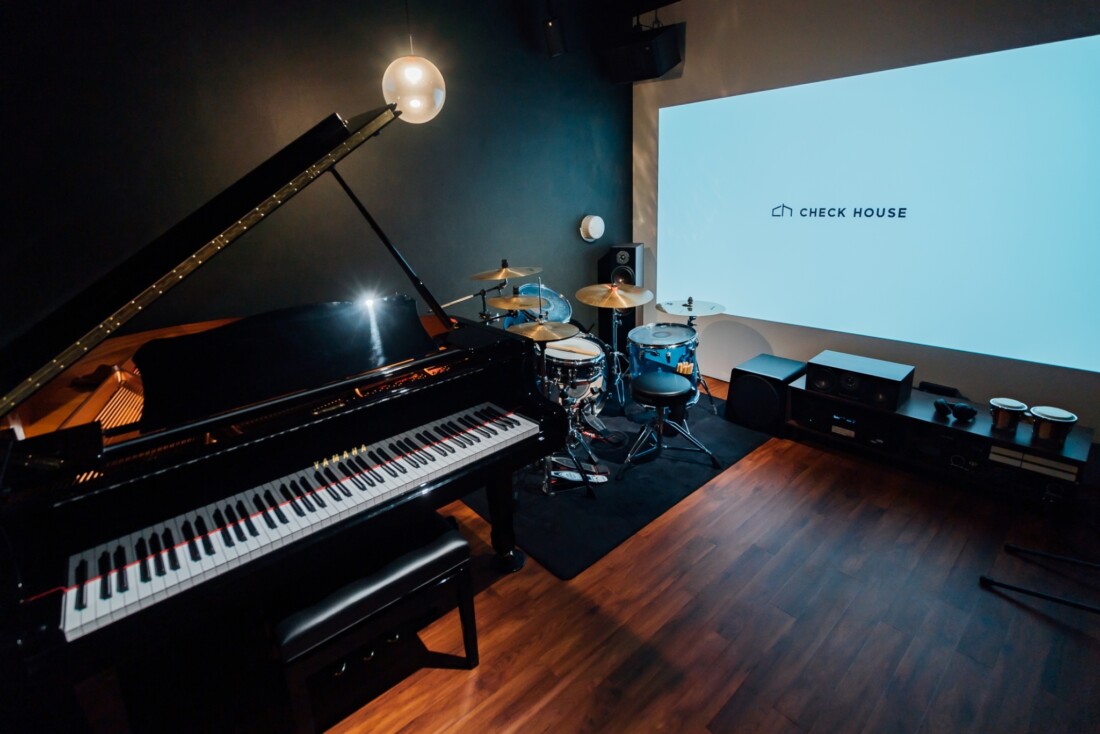 チェックハウス｜楽器がセットされた音楽ルーム。グランドピアノとドラムセットが置かれており、防音仕様で演奏に集中できる空間になっている。