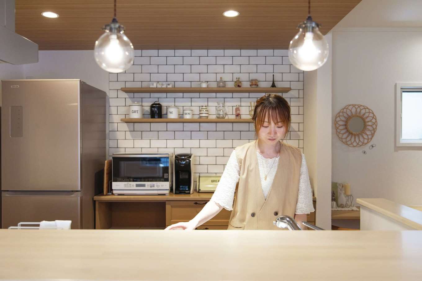 ハートホーム【デザイン住宅、自然素材、間取り】キッチン背面はタイル張りの壁にディスプレイ棚をつけてカフェ風に。その下は造作収納になっている。木目の下がり天井でナチュラルな雰囲気を演出