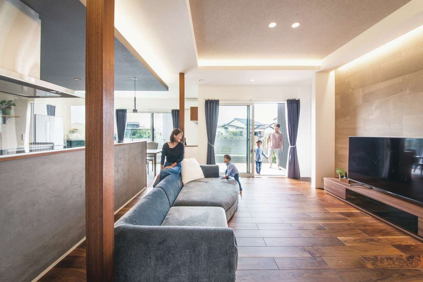 コットンハウス【デザイン住宅、子育て、省エネ】間接照明が映えるLDKには、リゾートホテルのような開放感が広がり、家の中にいてものびのびと過ごすことができる。南面の掃出窓の外にはデッキと庭があり、いっそう空間の広がりを感じさせる。キッチンの腰壁のモールテックスは夫妻のこだわり。コンクリート調のエコカラットともベストマッチ