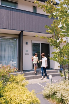 アプローチに敷かれた黒いタイルのようなものは、コンクリートに色を混ぜたもの。リーズナブルながら、落ち着いた雰囲気を演出できる。玄関の階段をリビング側まで伸ばすことで、窓から室内に入れ使い勝手も向上