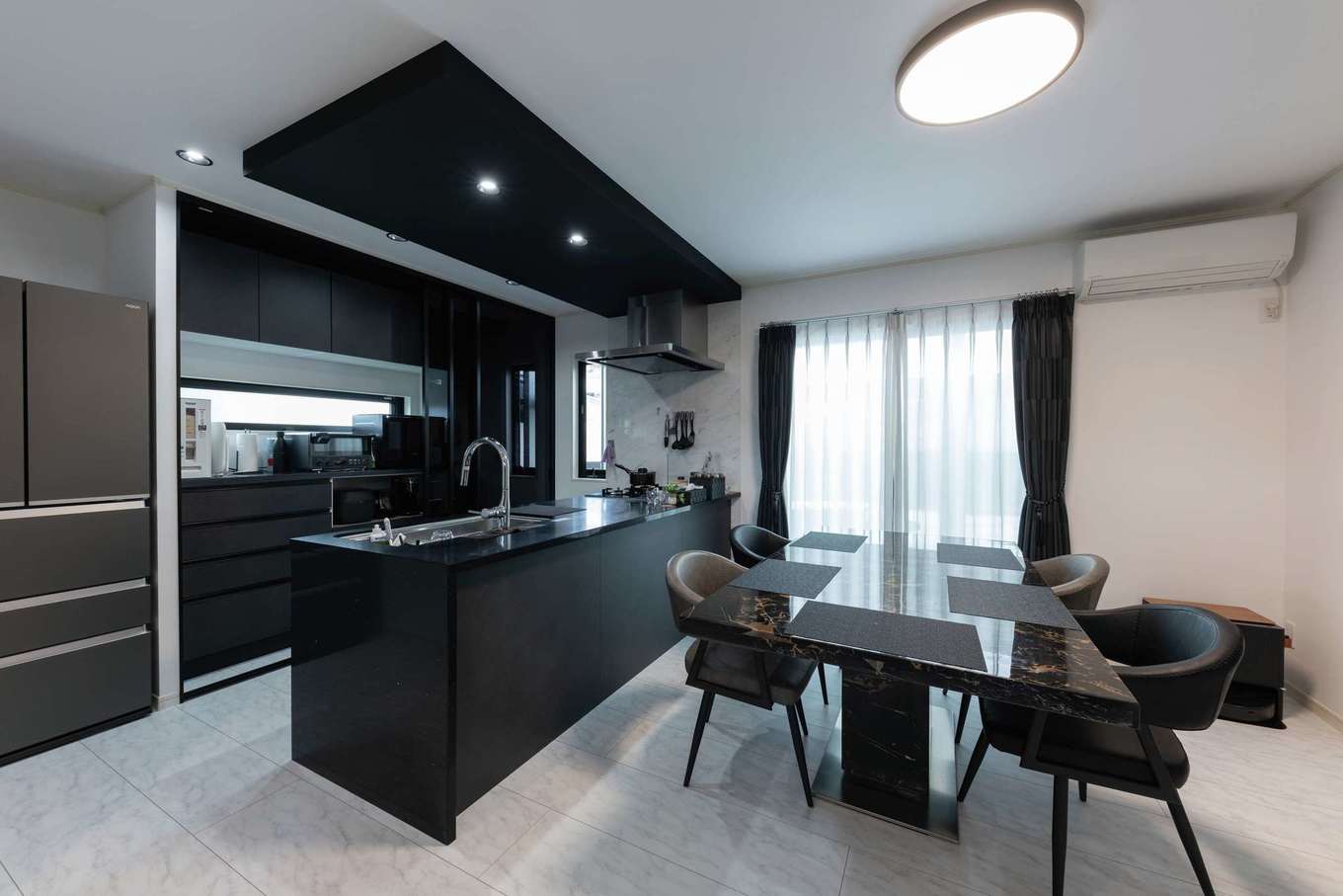 サンワ開発【デザイン住宅、収納力、ガレージ】モノトーンでまとめたDK。キッチンの天板と側面には、適度な光沢が上質感をもたらすクォーツストーンを採用した。奥の収納は半透明の引き戸で隠せるようになっていて、来客時などは生活感を抑えることができる