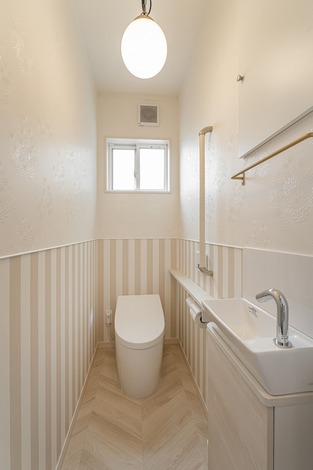 コンパクトながらも洗練されたトイレ空間。ストライプの壁紙がアクセントとなり、明るい室内を演出している。