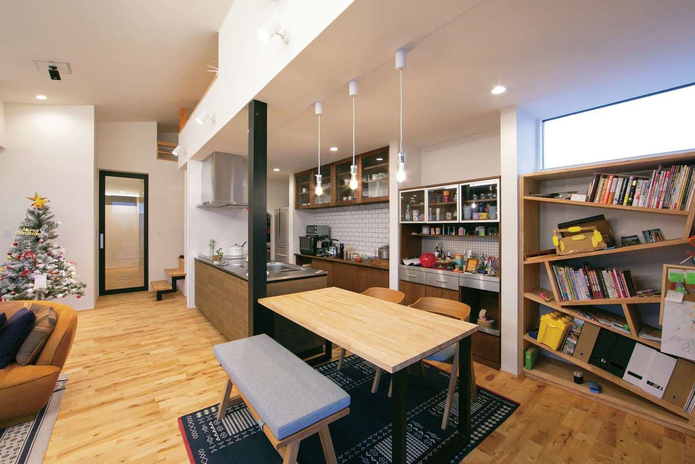 TENアーキテクツ 一級建築士事務所【デザイン住宅、建築家、平屋】ハーフ吹抜けのあるLDK。ダイニングテーブルをキッチンと横並びにすることで、家事効率が高まり、空間を広く使うこともできる。斜めに板を組み合わせた造作の書棚がインテリアのワンポイントに