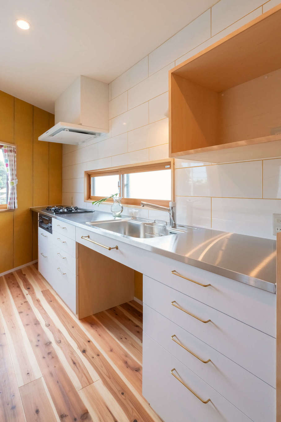 ALAIN（アラン）｜『ALAIN』のオリジナルデザインのキッチン。同社の提案で、壁には大判の白タイルを用い、目地を壁と調和するイエローで仕上げたのがこだわり。目線の高さで電子レンジが使えるよう、造作の専用棚を設けてある。シンクの下にはゴミ箱を収納するスペースを確保