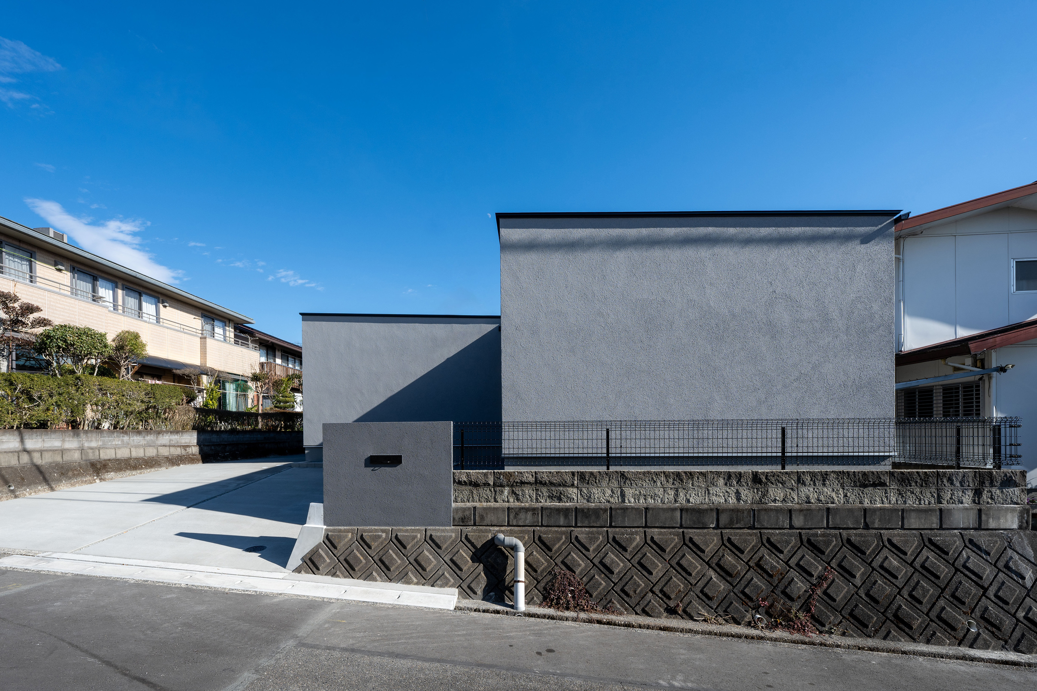ハウスプラン（R＋house沼津・富士）【間取り、建築家、平屋】開口部のない、グレーの塗り壁の外観が、周囲に住まい手のセンスを伝える。道路真正面からは2つの箱が並んでいるかのように見える
