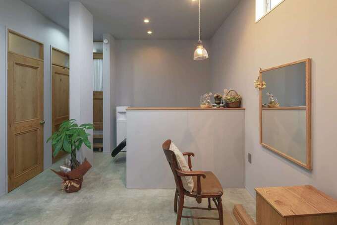 美容サロン内の壁と天井は淡いグレーの塗装でフラットに仕上げてある。ムラの無い美しい仕上がりに職人の技術力の高さが感じられる。カウンターの奥に自宅へ通じる出入口がある