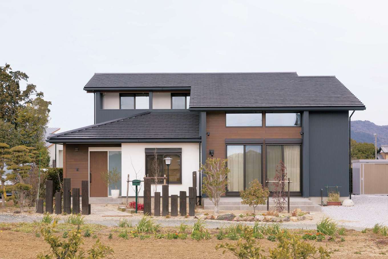 神谷綜合建設 カミヤの家【収納力、間取り、スキップフロア】極力メンテナンスフリーにするべく、外壁にはガルバリウム鋼板を多用。手の届く範囲だけ白壁を導入し、メリハリのあるデザインに。玄関アプローチや枕木を立てた塀など、外構は自分たちで手作り