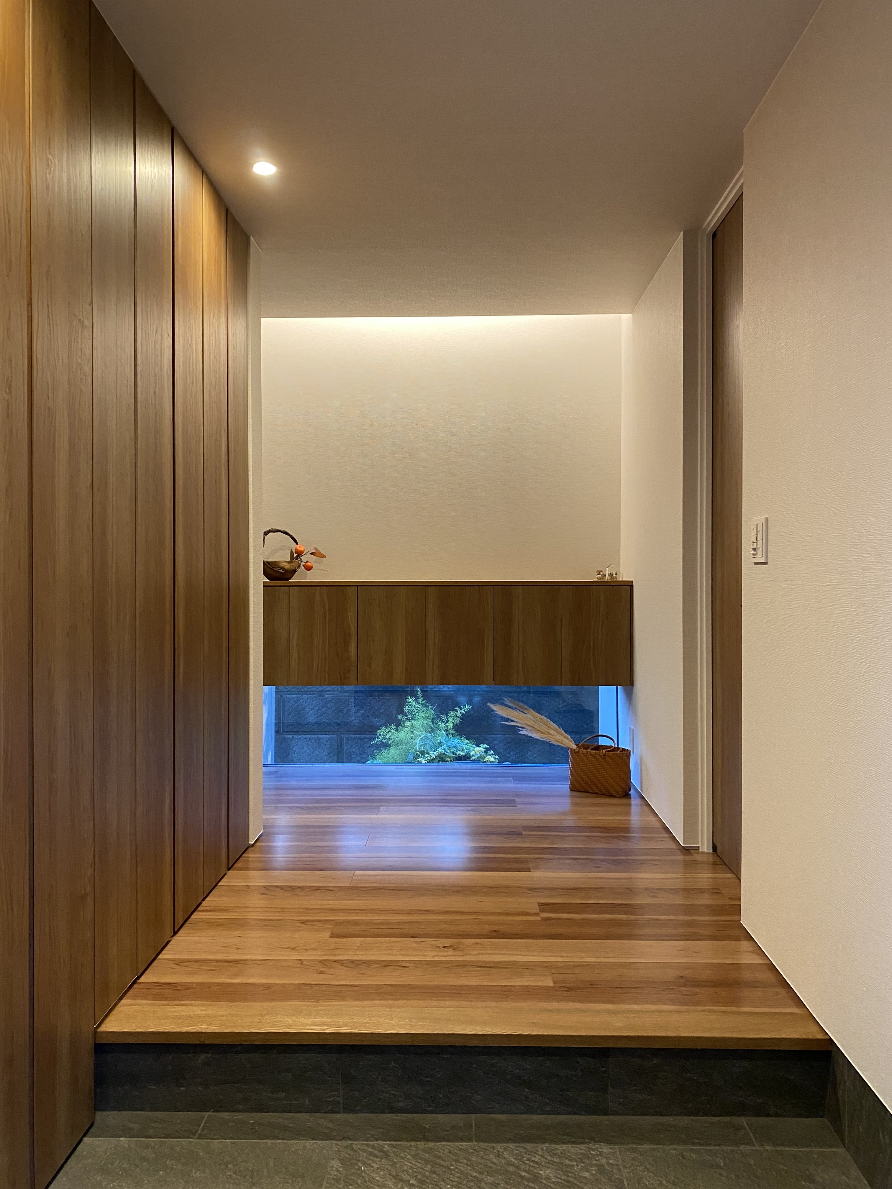 安田住宅｜安田建築設計室｜シンプルで洗練された玄関ホール。無垢材のフローリングと間接照明が、落ち着いた雰囲気を演出する。シューズボックスや小物の収納スペースも確保されている。