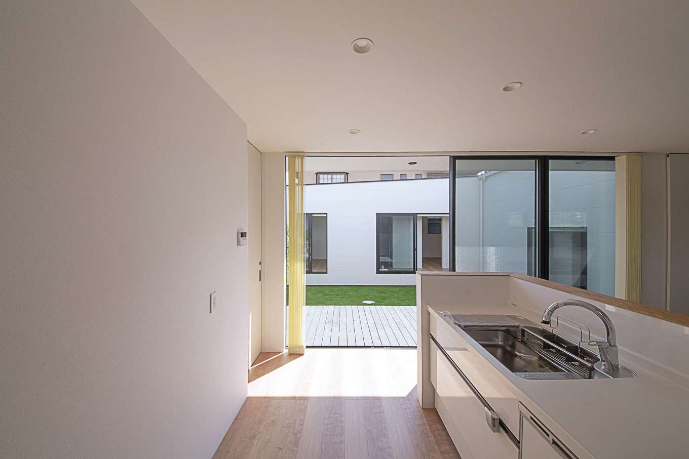 インフィルプラス【デザイン住宅、建築家、インテリア】リビングダイニングに向いた対面キッチン。ワークトップが隠れるように腰壁を高くしてある。サイドの掃出し窓から中庭と子ども部屋の様子を見渡せる
