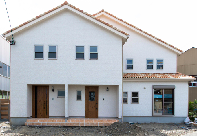 ホワイト系の壁にオレンジの瓦が映える外観。間取りの工夫で、明るさが必要な居住スペースを建物奥に配置し、幹線側の開口を必要最小限にしている