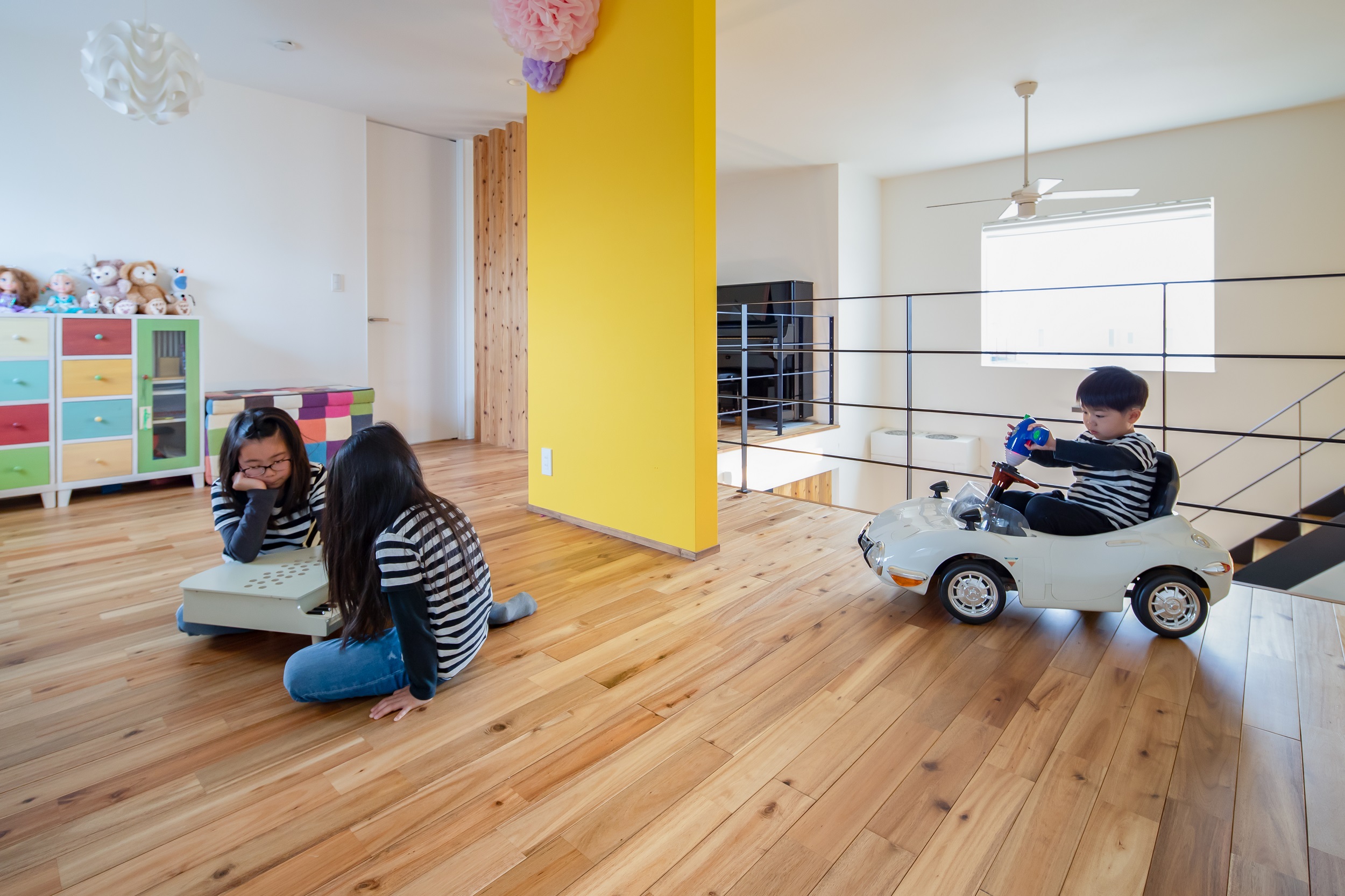 S.CONNECT（エスコネクト）【デザイン住宅、子育て、建築家】2階のフリースペースで元気いっぱいに遊ぶ子どもたち。イエローのアクセントウォールは目隠しにちょうどいい位置にあり、圧迫感がないサイズが絶妙。無垢の床の温もりが素足にやさしく、座り込んだり、寝転がって遊んだりしても気持ちいい