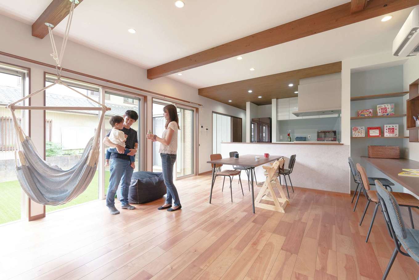 ホームプラザ大東【デザイン住宅、子育て、収納力】大きく開かれた窓から光と開放感が運ばれ、実際の広さ以上の大らかさで満たされるLDK。梁やカウンターには濃いブラウンを選び、落ち着きを添えた。床は掃除のしやすいタイプを選択。建具も溝や段差のない吊り戸が使われている。展示場を巡っている際に気に入ったハンモックを採用