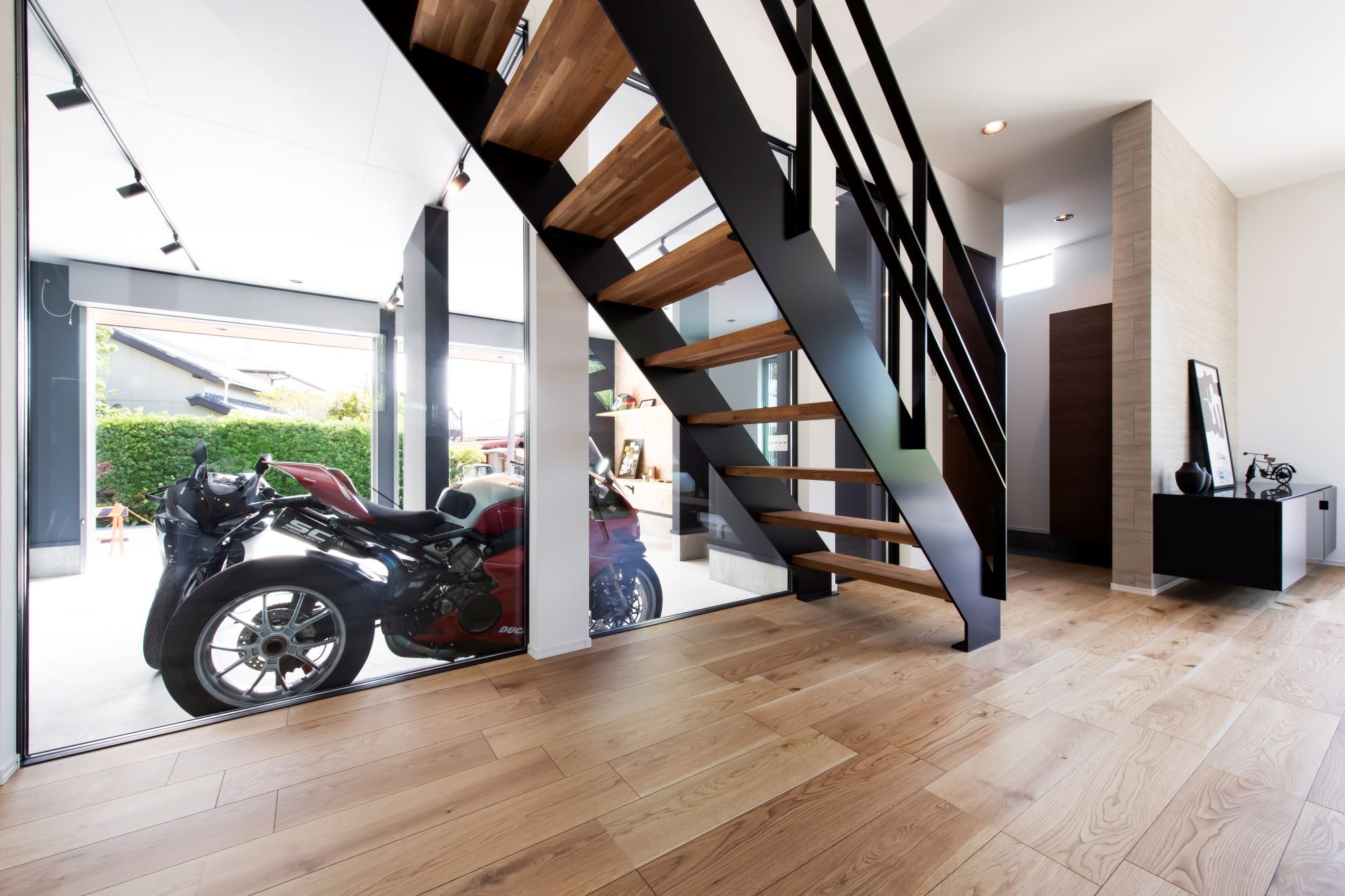 スズイチ｜モダンなデザインの階段。ガラスの壁越しにバイクが見え、インテリアとしての存在感を加える。