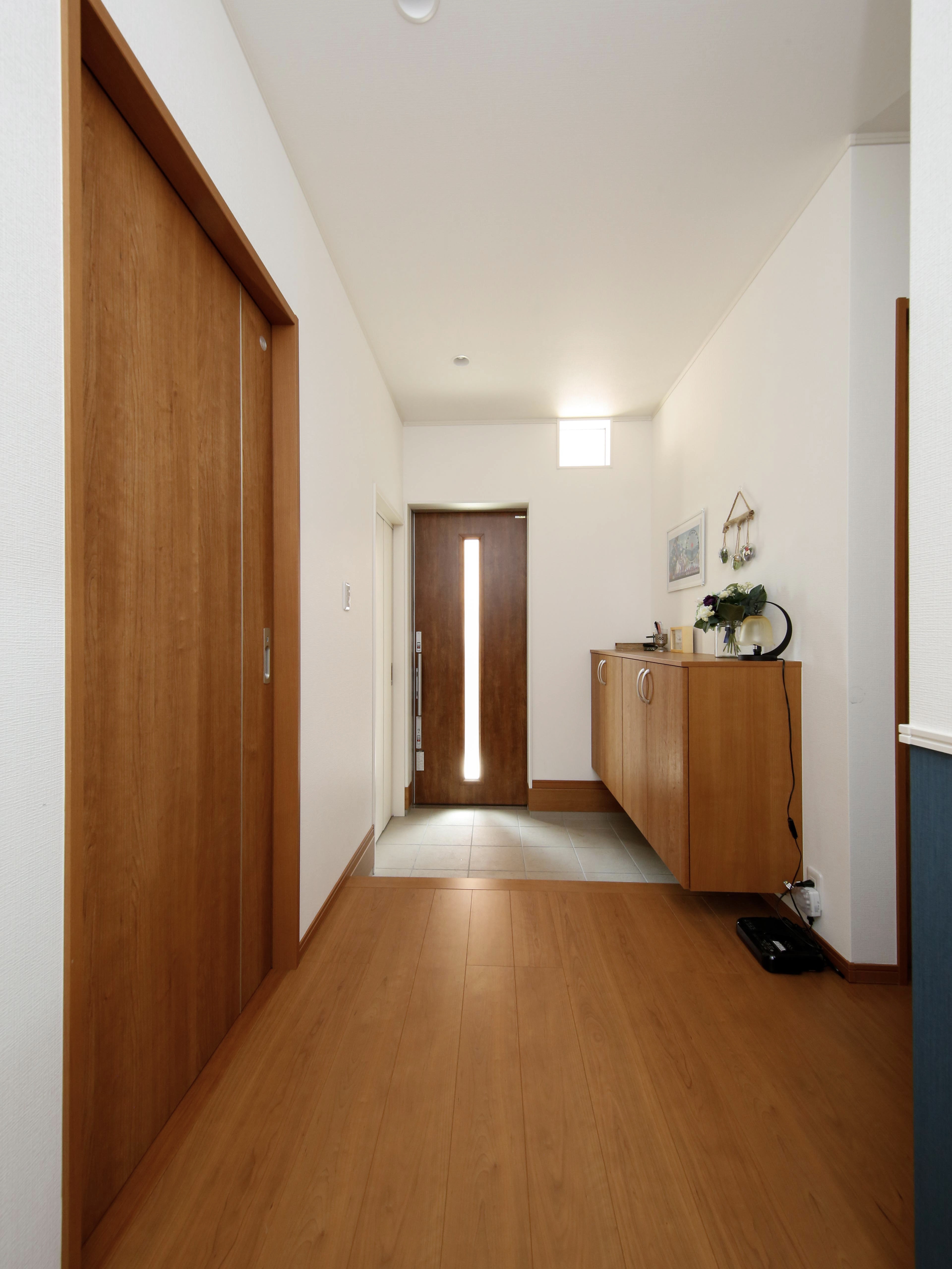 エスホーム｜木製の床材とシンプルなインテリアが調和した玄関ホールは事務所と居住スペース。玄関扉はベビーカーがそのまま入れるように引き戸を採用。