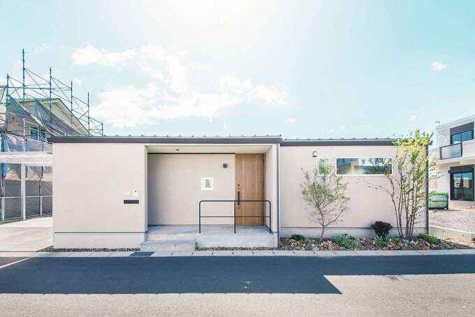 道路側から見た平屋の外観は、端正な長方形のフォルム。中央に玄関を置いてポーチを広く取ったシンプルなファザードに、ブラックアイアンの手すりがアクセントをつけている