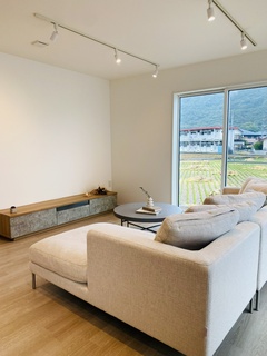 大きな窓から自然光が差し込む、開放的なリビング。シンプルなインテリアがリラックスした空間を演出している。ただし、広々としたソファが快適さを提供。