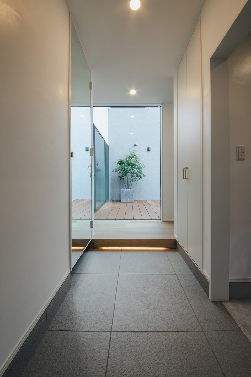 nattoku住宅【デザイン住宅、自然素材、間取り】玄関ドアを開けるとFIX越しの中庭へと目線が抜けていく。全身を映す姿見を設置したことで、空間がより広く見える