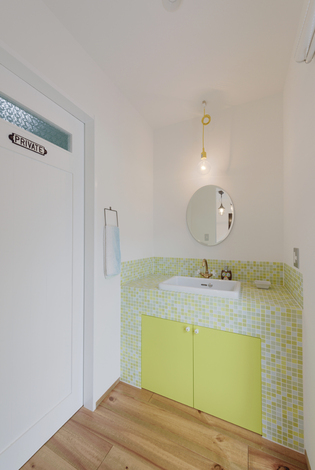大胆なカラーを用いた洗面スペース。イエローの扉の回りにモザイクタイルをあしらってキュートにコーディネート