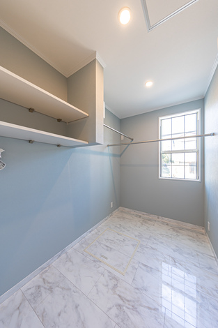 明るい窓から自然光が差し込むウォークインクローゼット。広々とした空間に充実した収納棚とハンガーポールが設置されている。