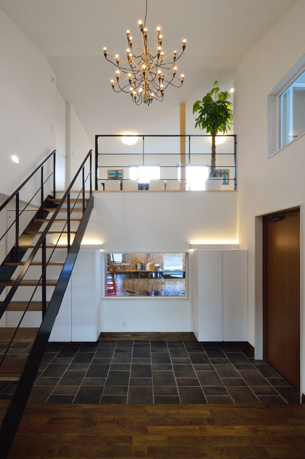 SEIEN ARCHITECT【デザイン住宅、建築家、インテリア】オープンな吹抜けの玄関。土間をまたぐようにストリップ階段を大胆に架け、玄関収納の合間にインナーガレージの見える大きなフィックス窓を配置