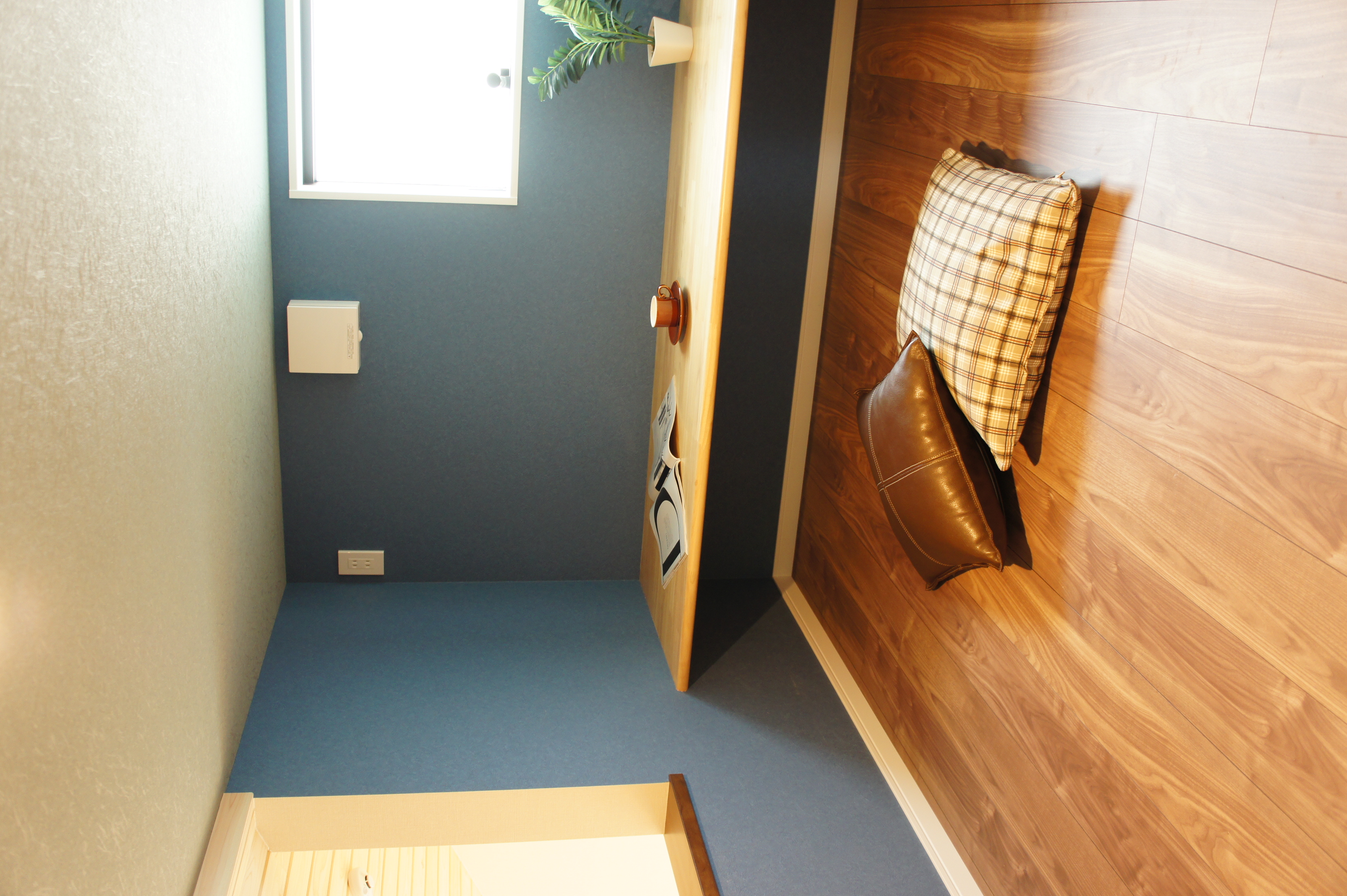 小野田産業～designers house project～｜コンパクトで居心地の良いフリースペース。低めの天井と壁際のデスクがあり、趣味や読書の時間を楽しむのに最適な空間。クッションも置かれていてリラックスできる。