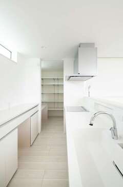 白一色でコーディネートされた清潔感溢れるキッチン。背の高いMさん夫妻に合わせ、キッチンと背面収納は高めに設置した。パントリーの一角には奥さまのパソコンコーナーも