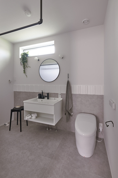 シンプルでミニマルなデザインのトイレ空間。壁に取り付けられた丸い鏡と間接照明が、洗練された雰囲気を演出している。観葉植物もアクセントとした清潔感溢れるスペース。