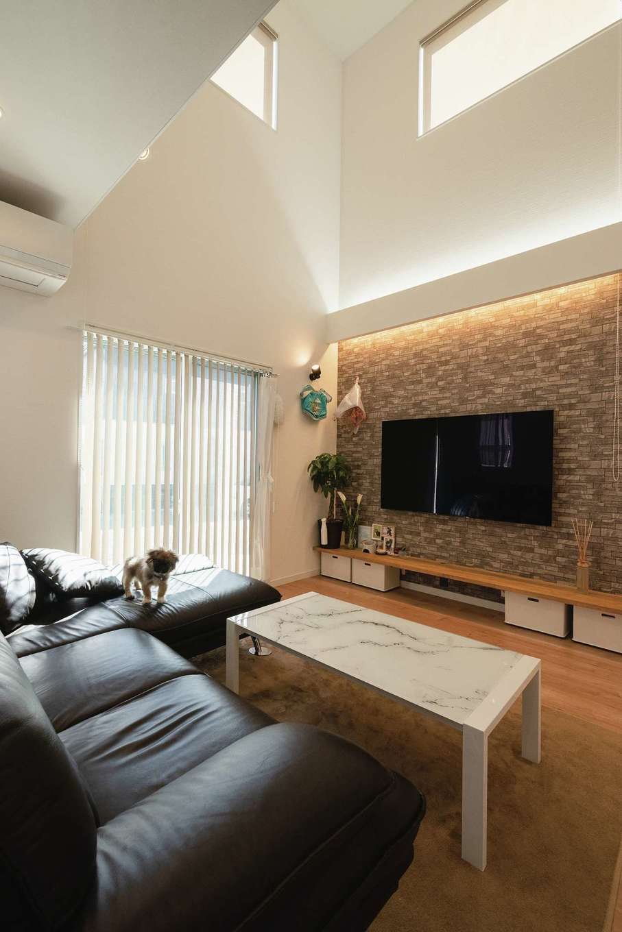 三和建設【趣味、間取り、ペット】テレビ背面をアクセントウォールとし、上下で色が異なる間接照明を設置。昼は上部2面の窓から降り注ぐ光で明るく、夜はがらりと雰囲気が変わって落ち着いた大人の空間に