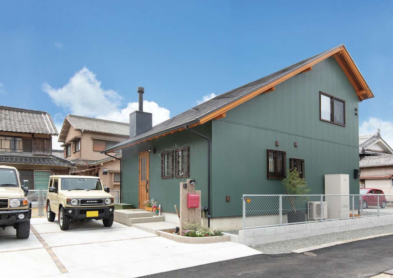 サイエンスホーム【デザイン住宅、自然素材、ペット】片流れの大屋根と薪ストーブの煙突が印象的なT邸の外観。モスグリーンの外壁に木製の軒天、玄関ドアがアクセントに