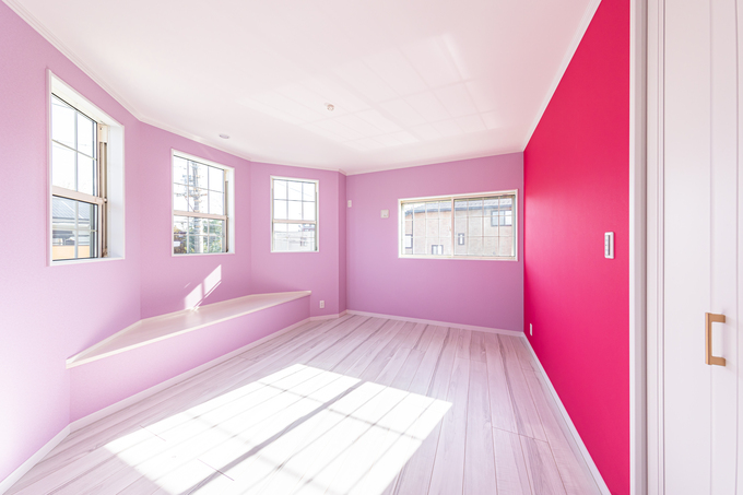 壁の一部が鮮やかなピンクで彩られた居室。複数の窓から入る自然光が、部屋全体を明るく照らしている。
