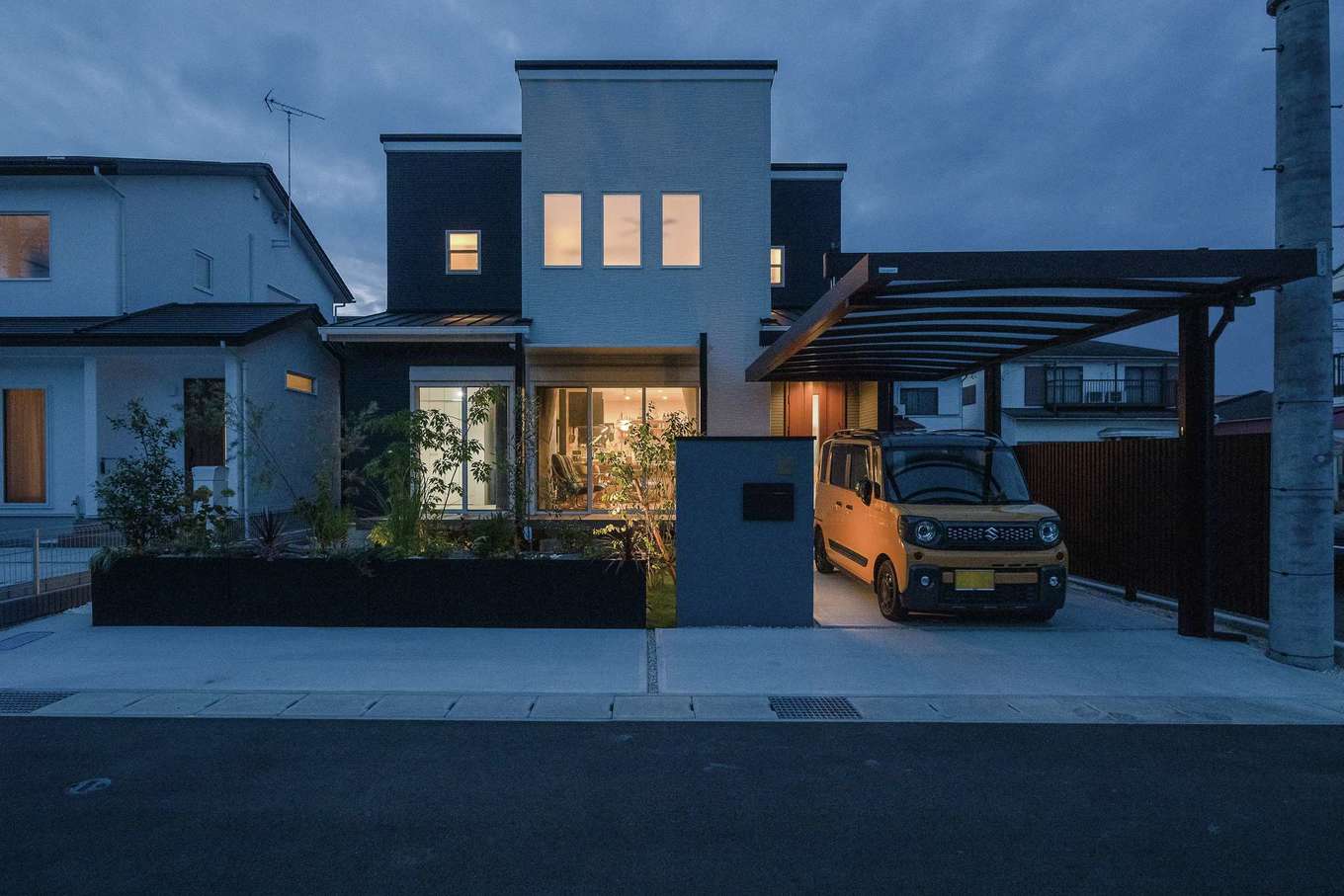 HAPPY HOUSE（山田工務店）【デザイン住宅、夫婦で暮らす、間取り】外観は「普通じゃないほうがいいですよね？」と提案されたモダンスタイル。植栽が通りからの視線を適度に遮り、外構に設えられた照明があたたかく迎えてくれる。駐車場から雨に濡れずに入れることも優先度の高い要望だった