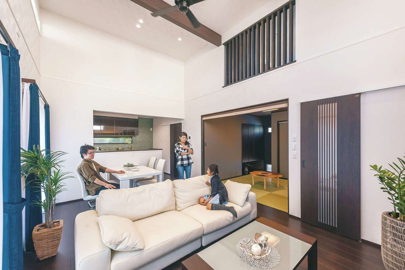 静鉄ホームズ【デザイン住宅、和風、間取り】和室はリビングと隣り合い、空間の横の広がりを作る。プリーツスクリーンで仕切ることも可能。吹き抜け上の格子は蔵とつながる窓。写真奥のキッチンの壁は、最初は真っ白の予定だったが、コーディネーターの提案で壁の一部にグリーン系の柄クロスを貼ってアクセントに。落ち着いた色味が和モダンなLDKに調和している