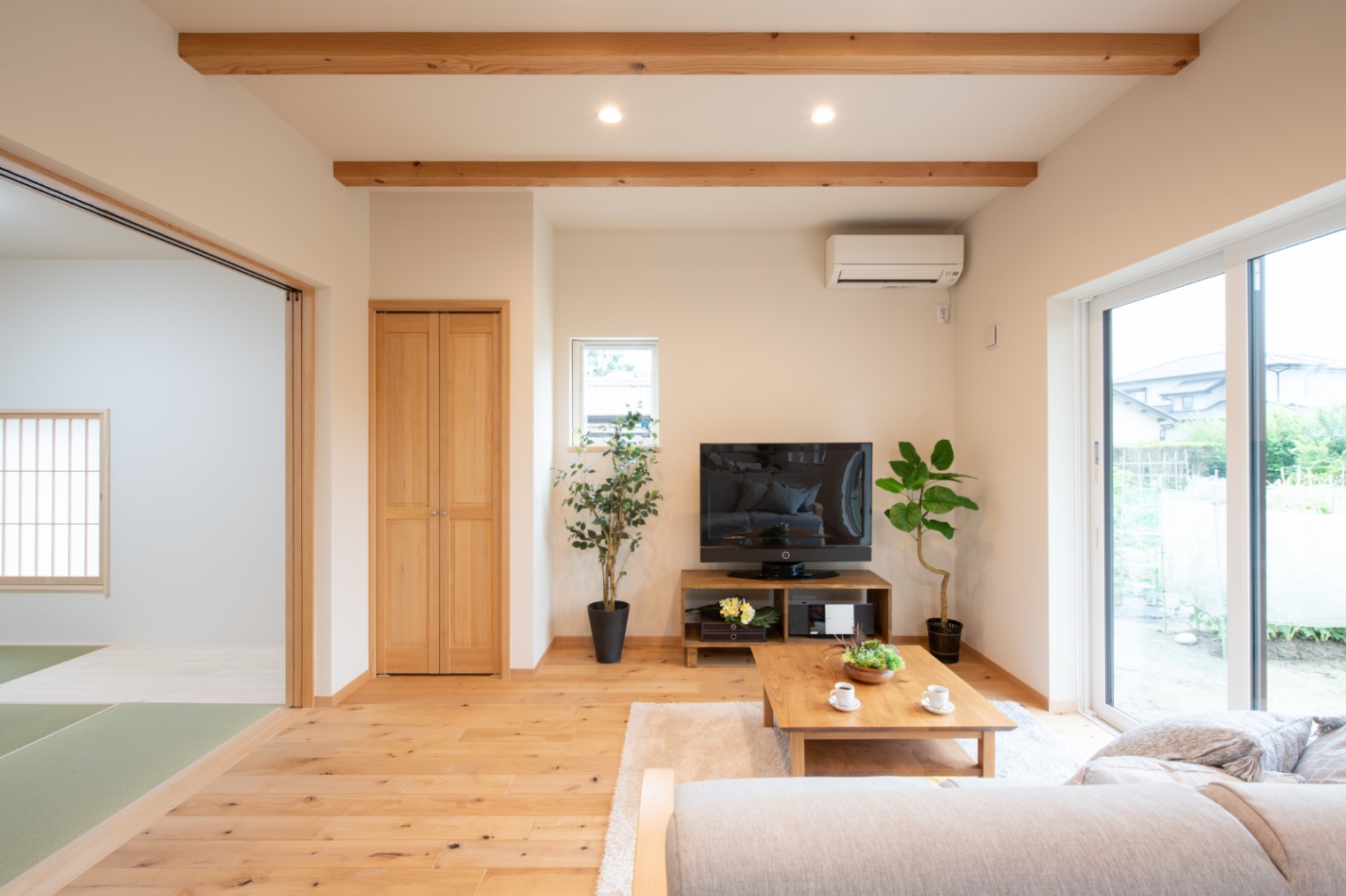 Sus∞Eco Home（サスエコホーム）｜明るい光が差し込むリビング。木材の温かみが感じられるフローリングと天井の梁が特徴。シンプルながらも心地よい空間が広がっている。