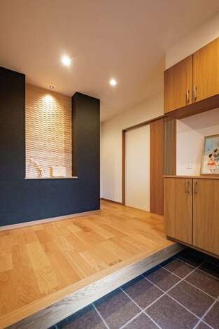 家の顔である玄関ホールには特にこだわった。正面に木のデザインウォールを張り、季節の花を飾るための棚も設置した。間接照明がニュアンスを与える