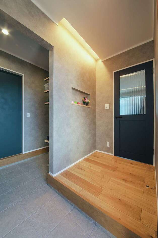 玄関はシックなクロスと間接照明でほっとする雰囲気。正面は土間収納、その先にファミリークロークが続く