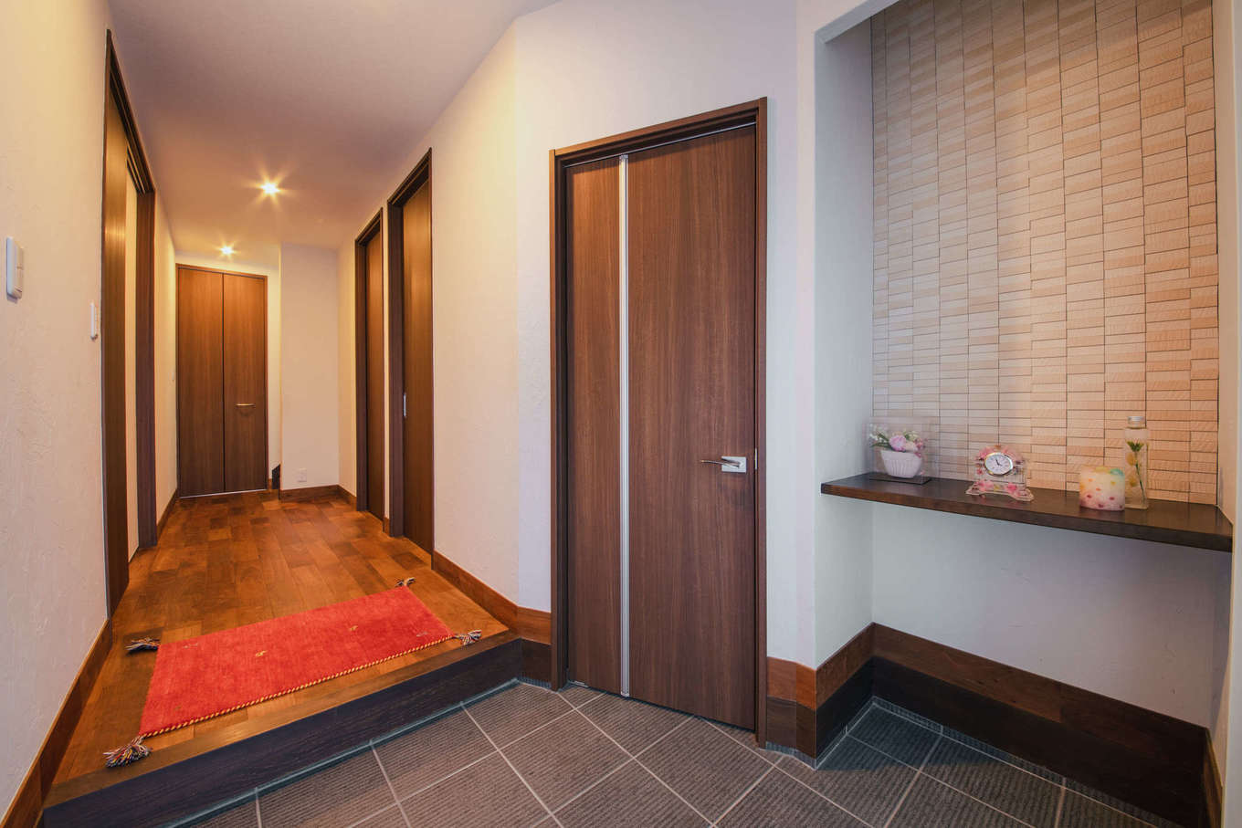 エフエフ住宅【子育て、和風、自然素材】小物を飾るカウンターとアクセントウォールが粋な玄関。ドアの奥には大容量のシューズクロークを設置