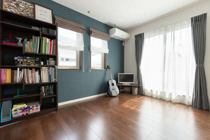 主寝室の一面にブルーのアクセントクロスを貼って、ご主人がギターを奏でる趣味部屋としても使っている。窓を開けると、変形に長くつながったベランダと直結
